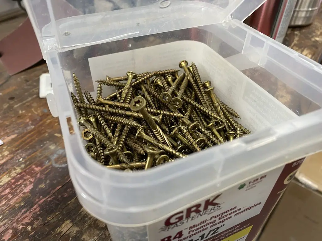 Box of gold screws on wooden surface.