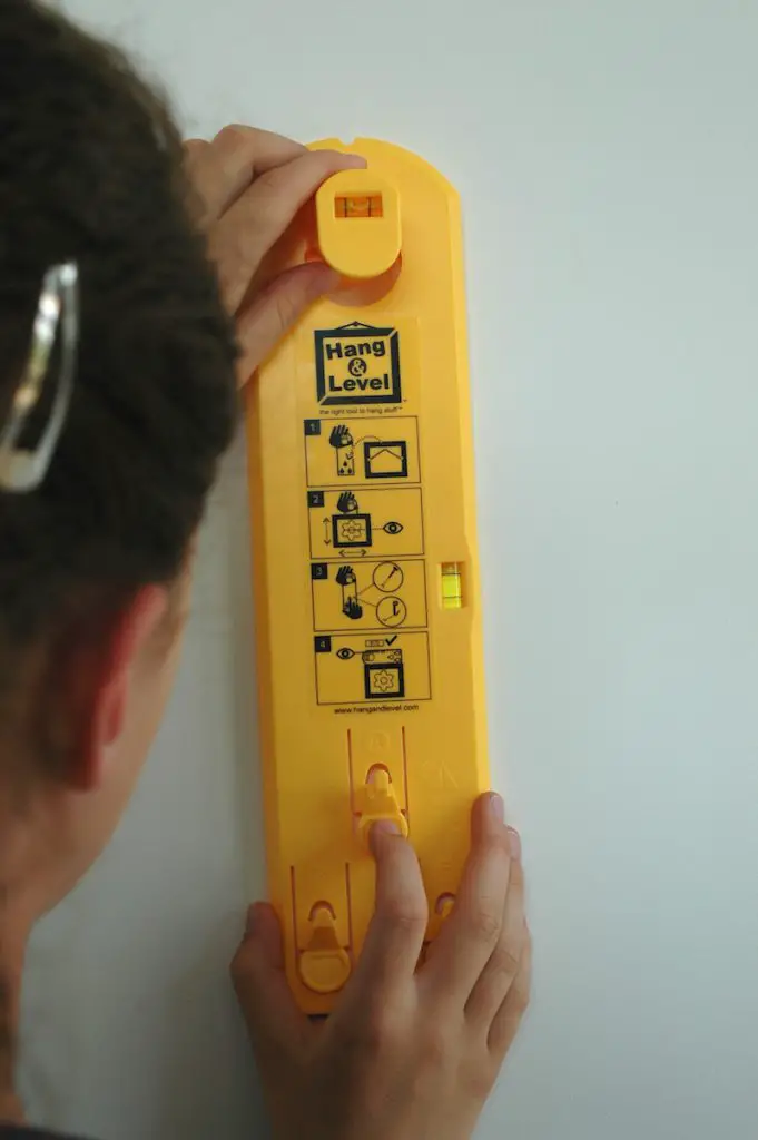 Person using yellow Hang & Level tool on wall.