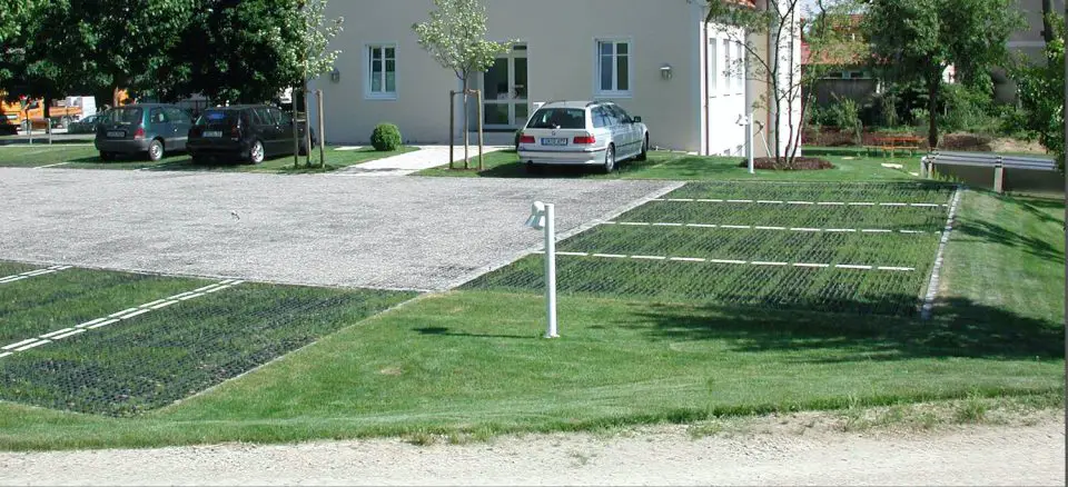 Grass-covered parking lot beside building with cars parked.