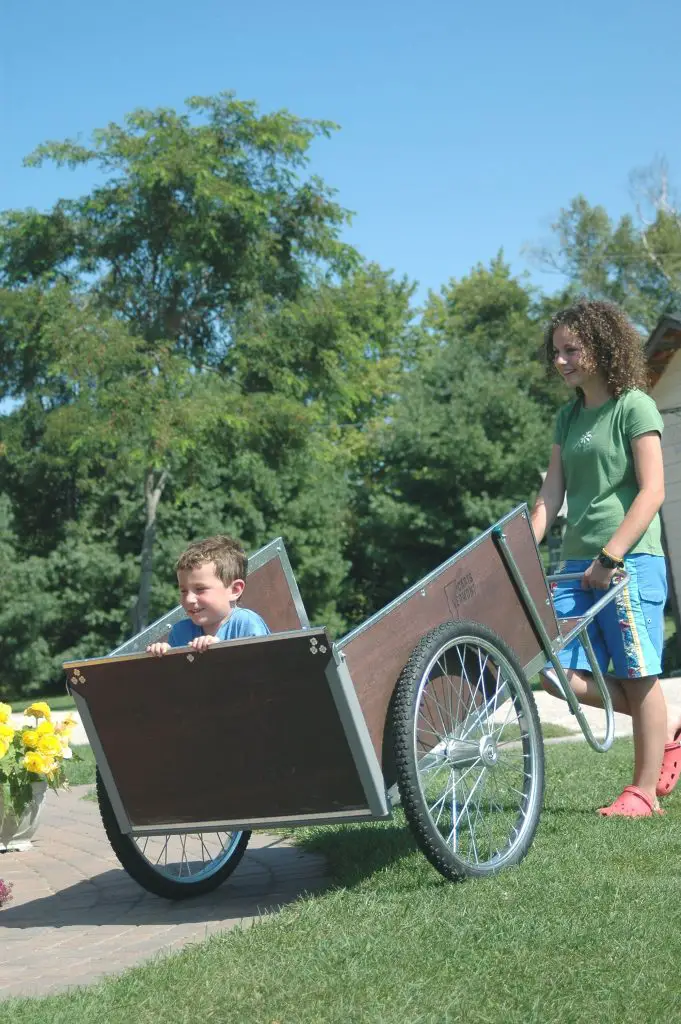 Child in wheelbarrow, teen pushing outdoors.