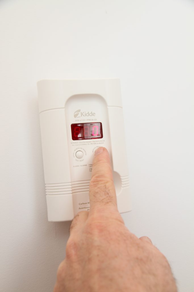 Person testing carbon monoxide detector with finger.