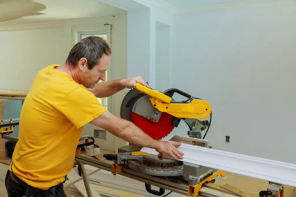 Man uses miter saw to cut wood indoors.