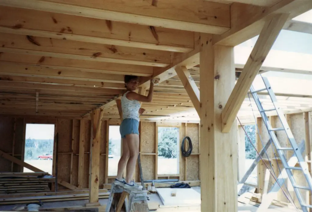 Person standing on ladder in wooden house frame