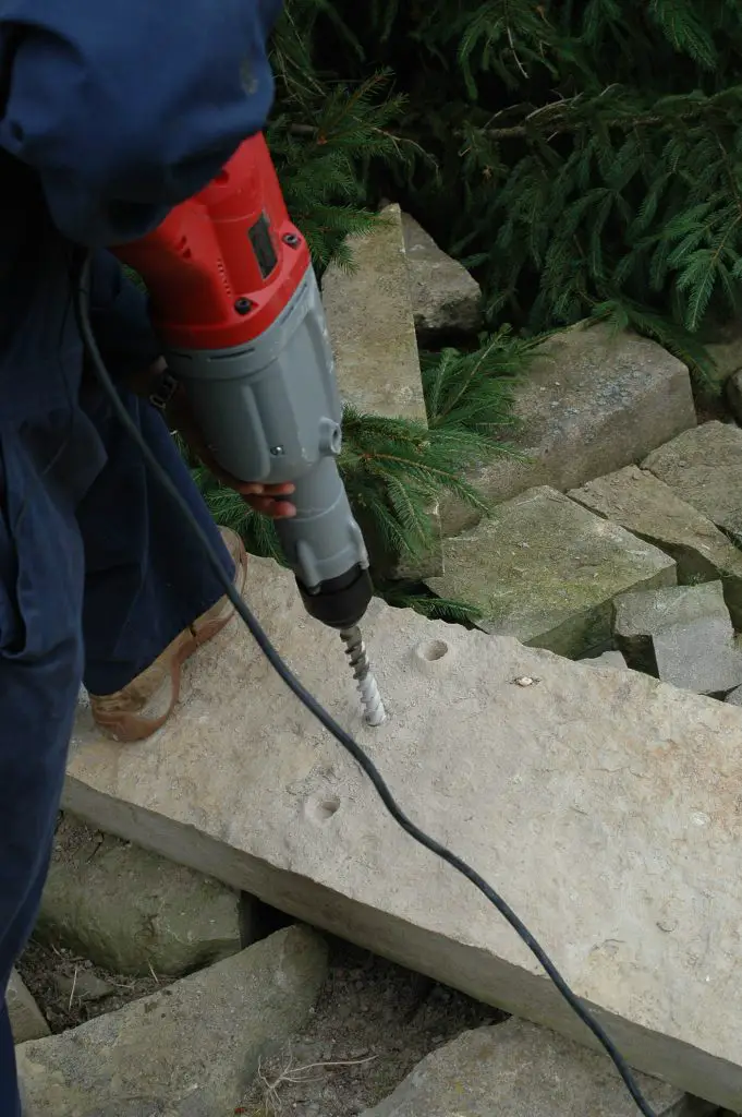 Person drilling holes in large stone block.