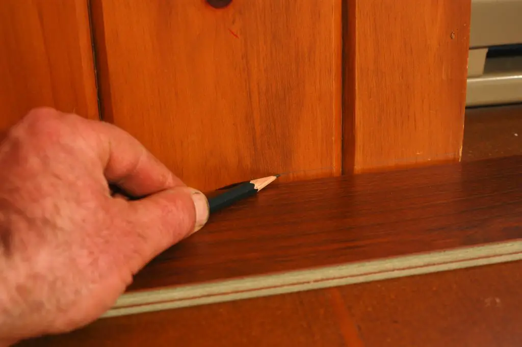 Marking baseboard corner with pencil on wood