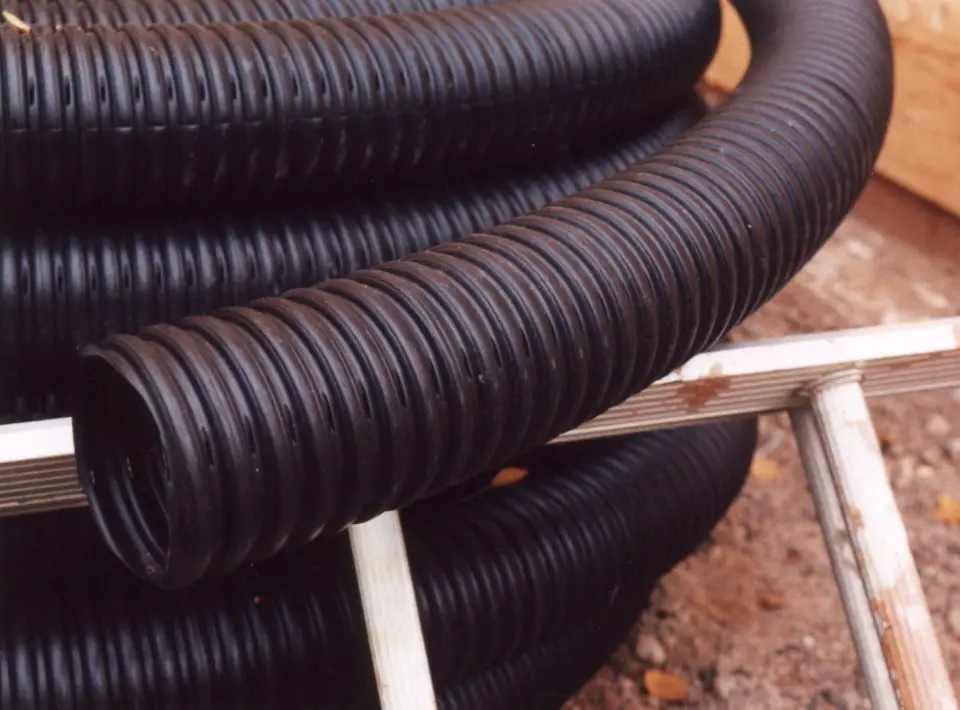 Coiled black corrugated drainage pipes on ground.