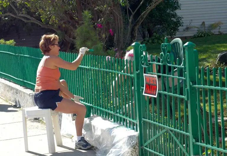 Woman painting a green fence in the garden.