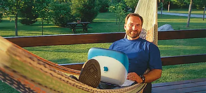 Man relaxing on hammock with laptop outdoors.