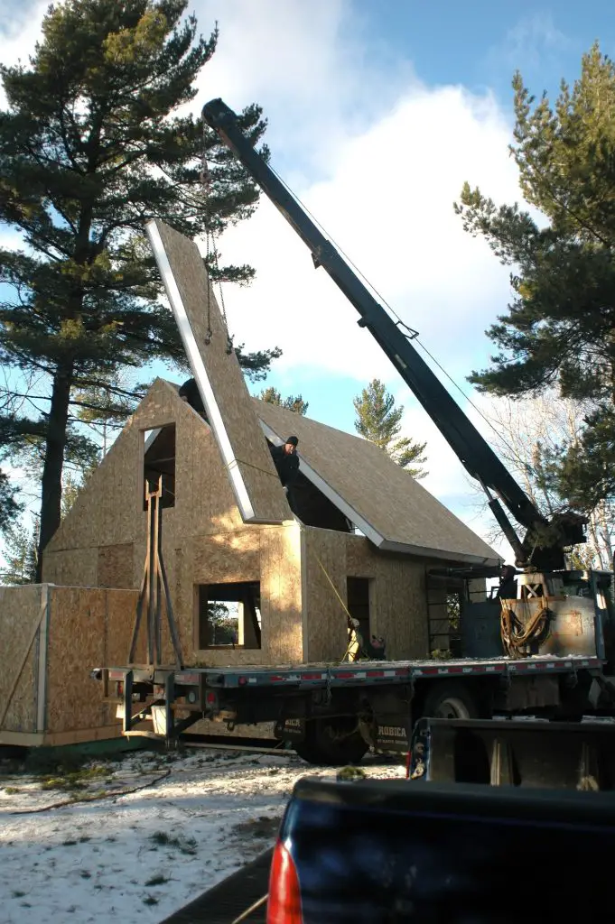 Crane lifting roof panel onto wooden house structure.