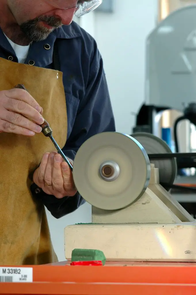 Man sharpening tool on grinding wheel machine.