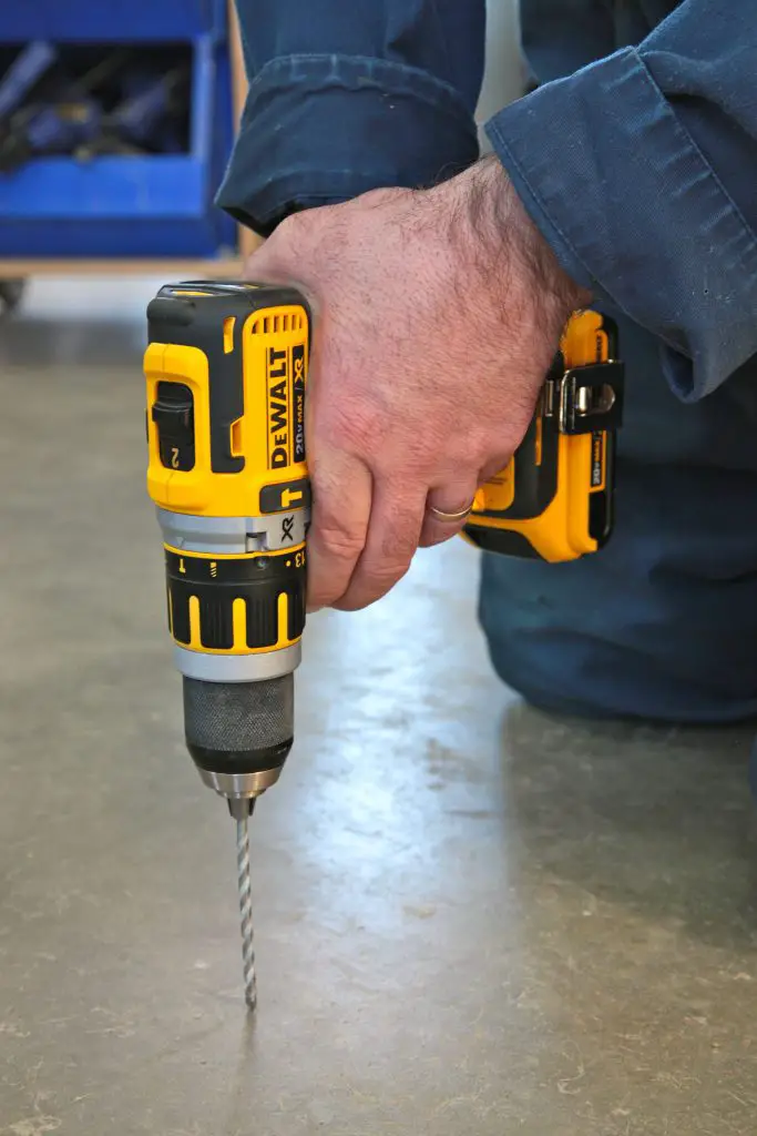 Person using a cordless drill on concrete floor.