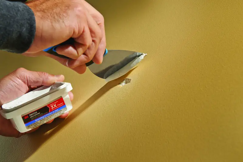 Applying wall patch with putty knife.
