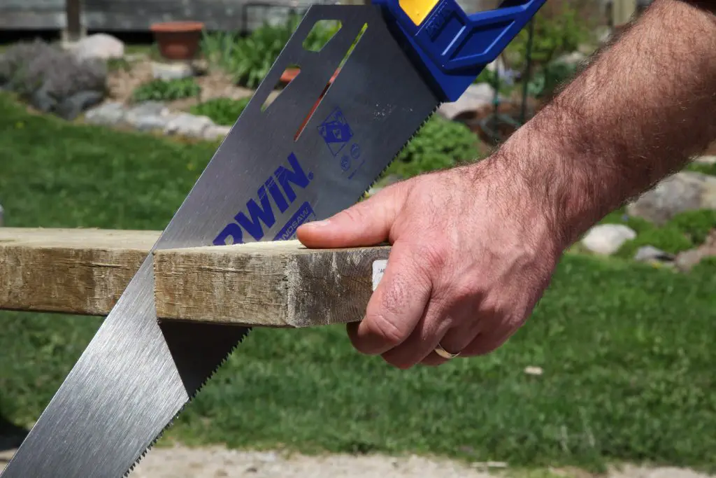 Person sawing wooden plank outdoors.