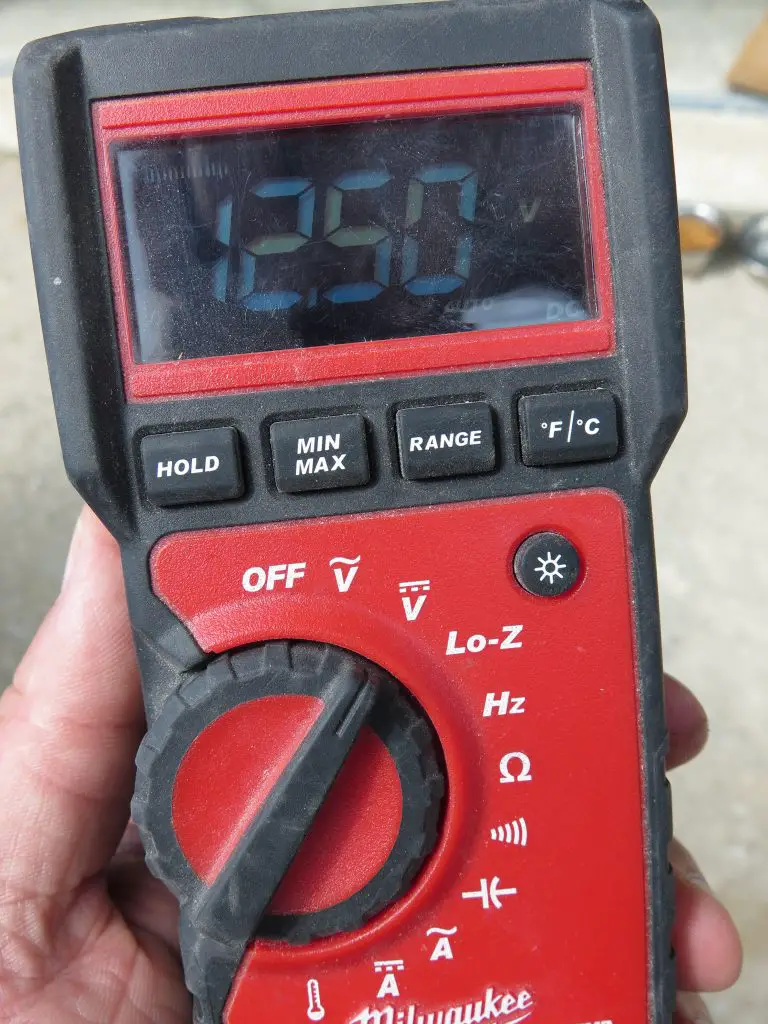 Hand holding digital multimeter displaying 1250 volts.