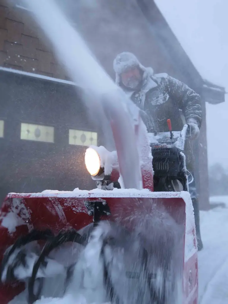 Person using snowblower during heavy snowfall.