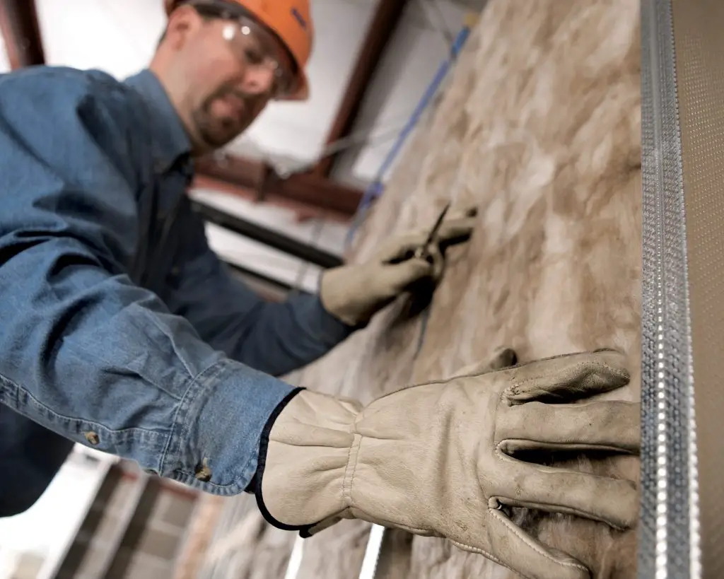 Worker installing insulation at construction site.