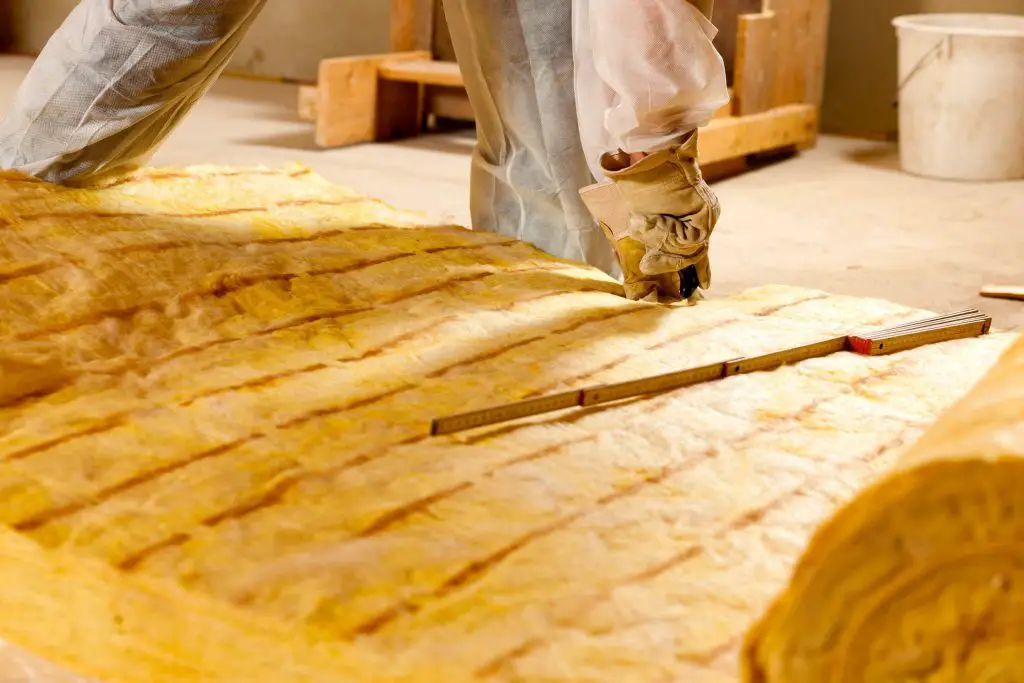 Worker measuring insulation material with folding ruler.