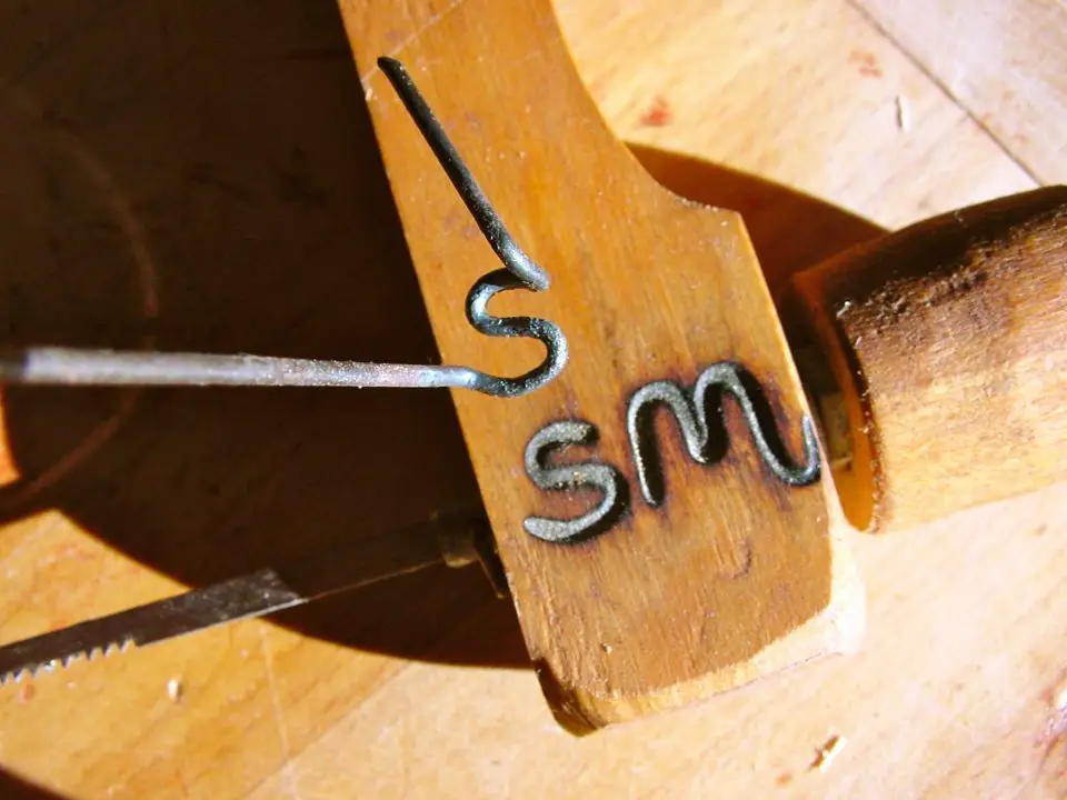 This is my homemade burning brand I use to mark my work and tools today. It’s made of 1/16″ piano wire, bent while heated red hot with a propane torch.