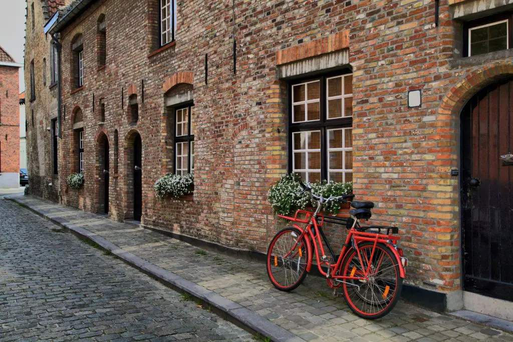 Red bicycle leaning against brick house with flowers.