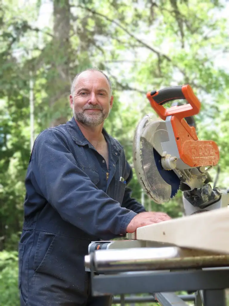 Man in overalls using a circular saw outdoors.