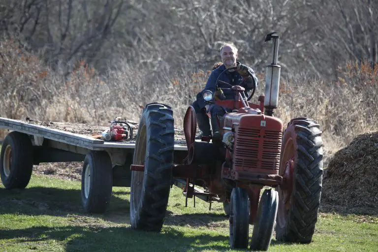 Person driving red tractor with wood trailer