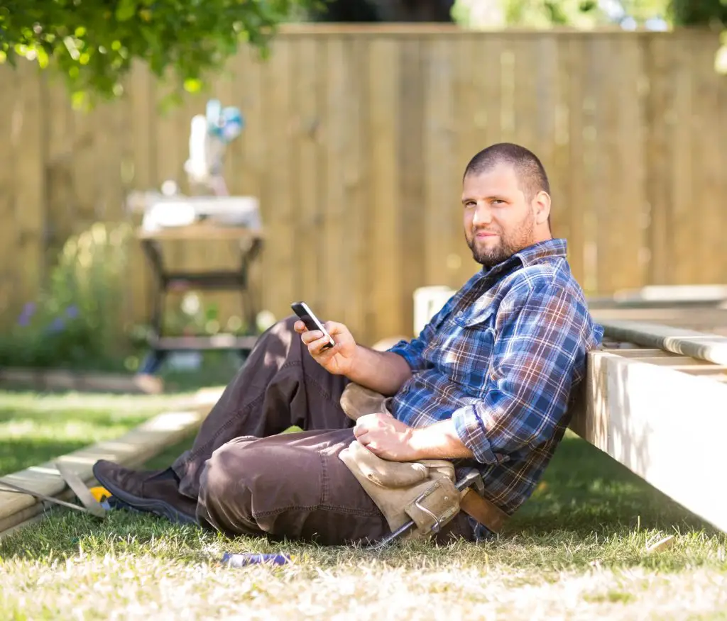 Construction worker sitting, using smartphone outdoors.