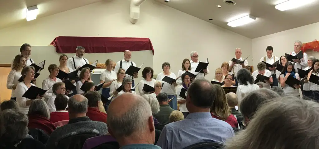 Choir performing for seated audience in community hall.