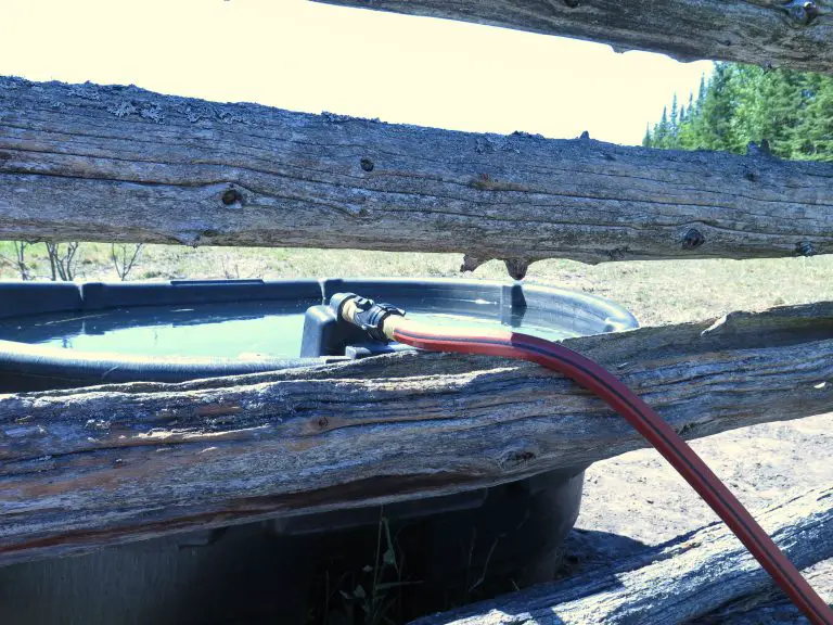 Water trough with hose behind wooden fence
