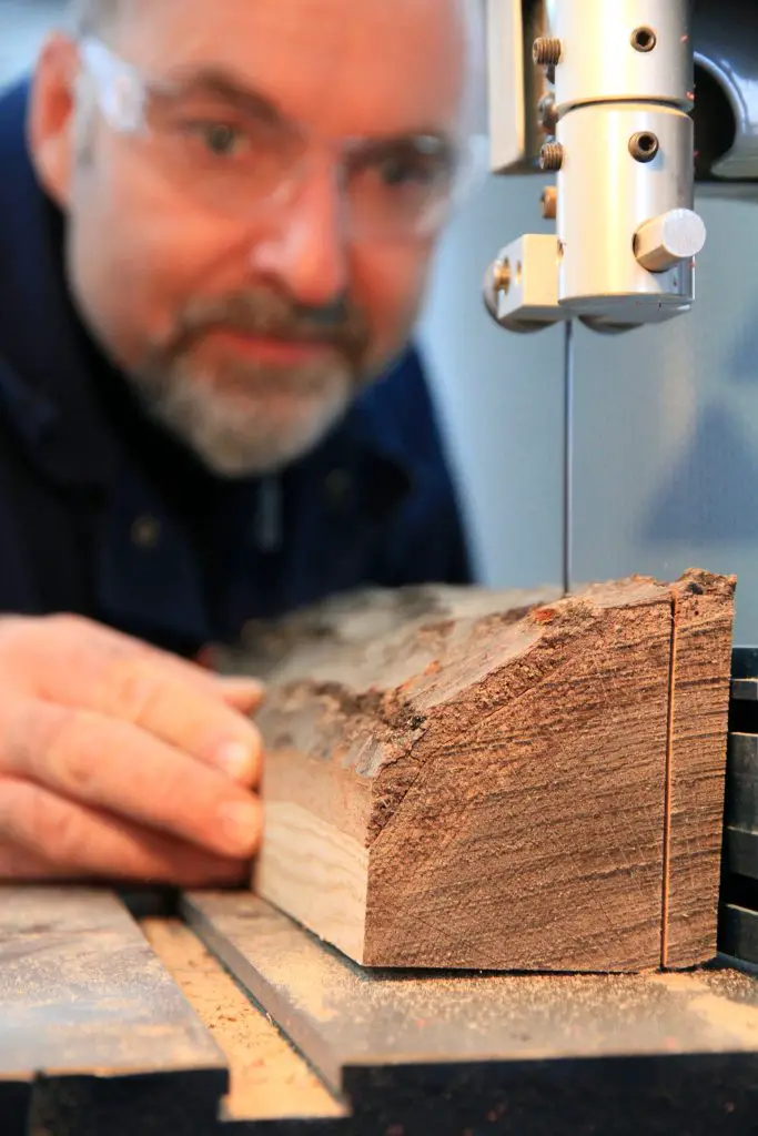 Man operates bandsaw cutting wood block.