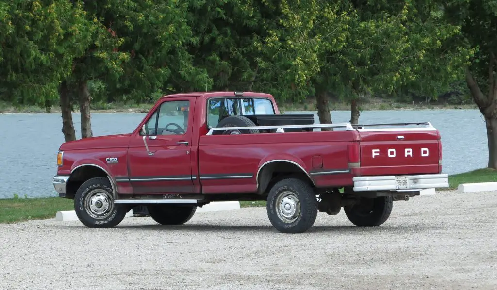 Red vintage pickup truck parked by lake.