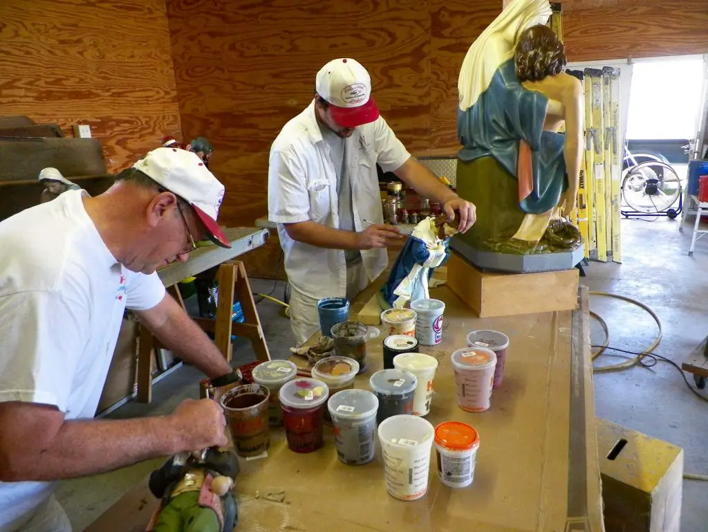 Artists restoring colourful religious statue in workshop.