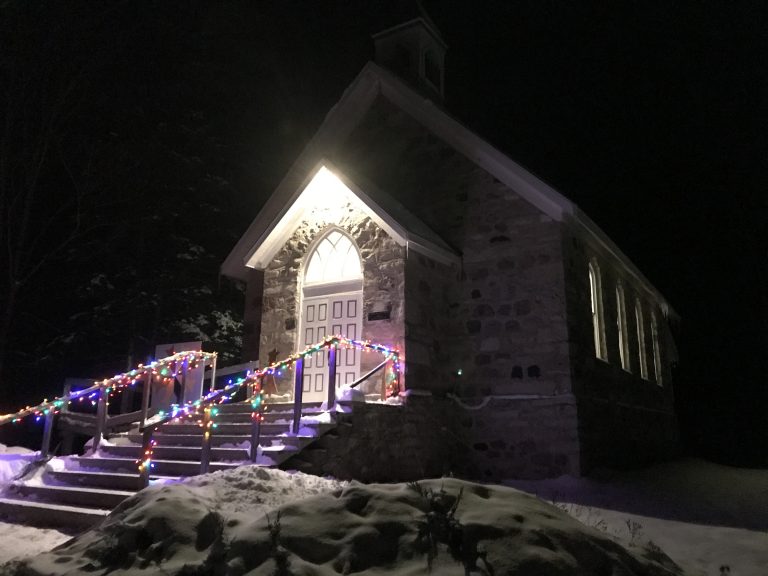 Stone church with colourful Christmas lights at night.