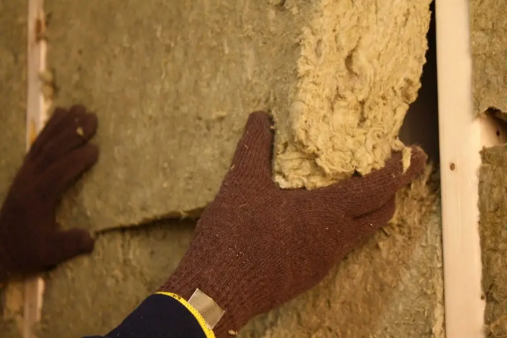 Installing wool insulation in wall cavity.