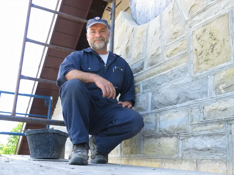 Construction worker kneeling beside stone wall and scaffolding.