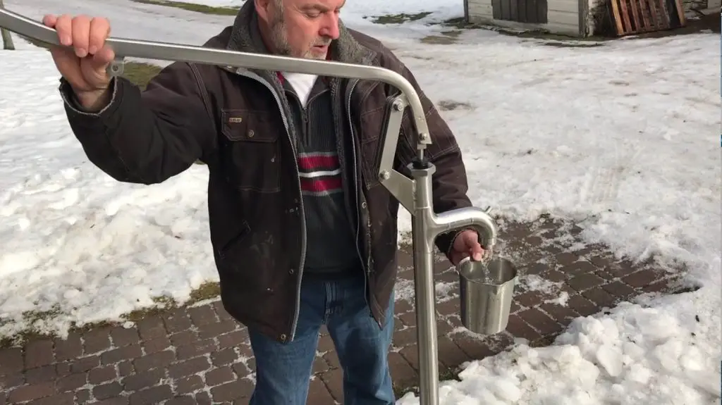 Man using outdoor water pump in snowy yard.