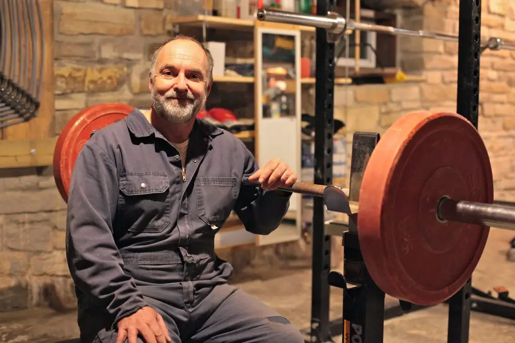 Man in workshop smiling beside weights equipment.