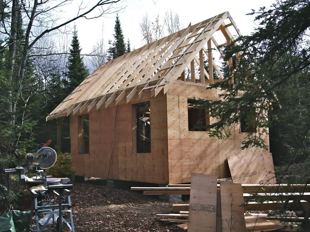 Unfinished wooden house in forest clearing.