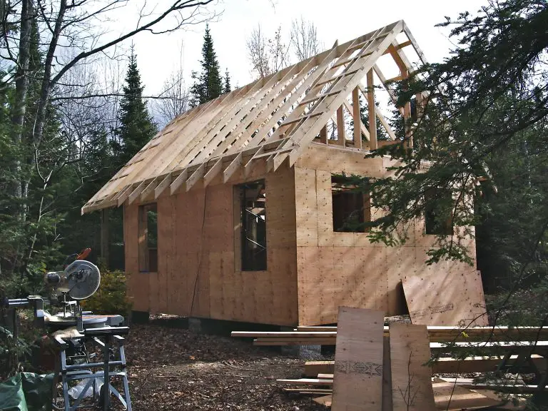 Unfinished wooden house in forest clearing.