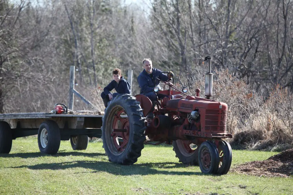 Two people driving a vintage red tractor outdoors.