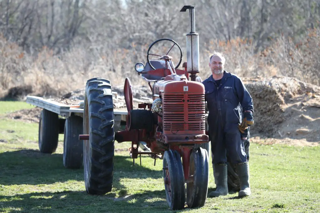 Farmer standing beside a red tractor in field.