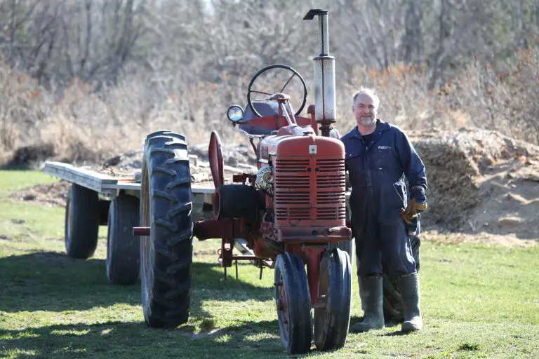 Farmer standing beside a red tractor in field.