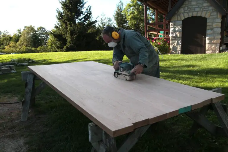 Woodworker sanding large wooden board outdoors