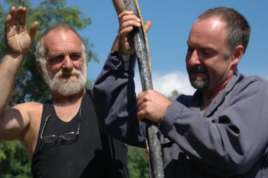 Two men working together outdoors, holding a pole.