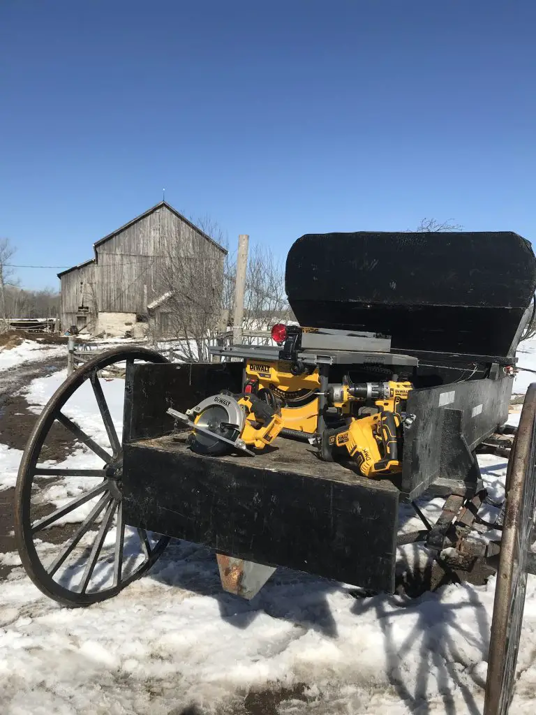 Yellow power tools on black wagon, snowy field, barn.