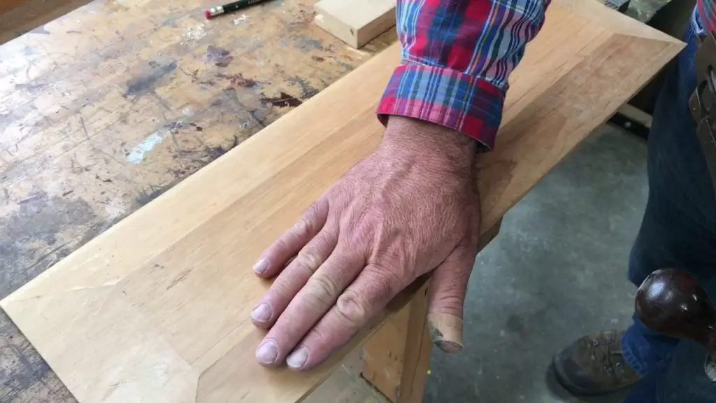 Carpenter's hand on wooden plank in workshop.