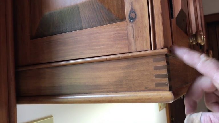 Hand pointing at wooden dovetail joint on furniture.