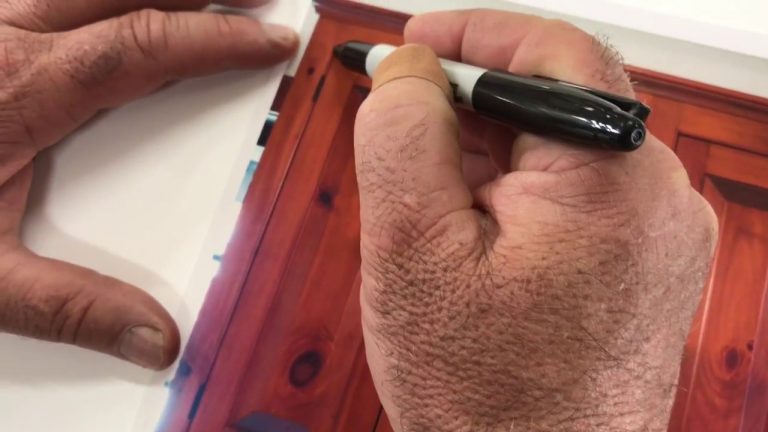 Person marking red wood print with black pen.