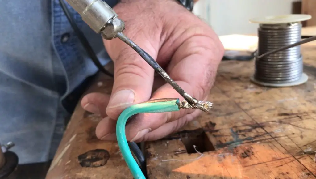 Person soldering wire on workbench.