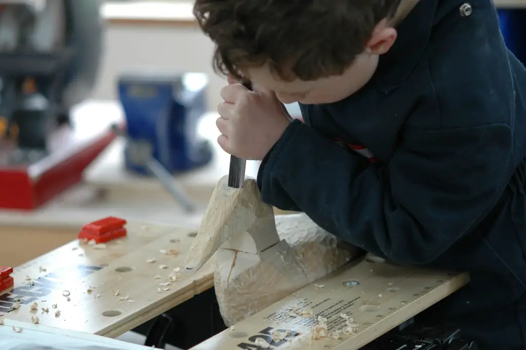 Child carving wood sculpture on workbench.