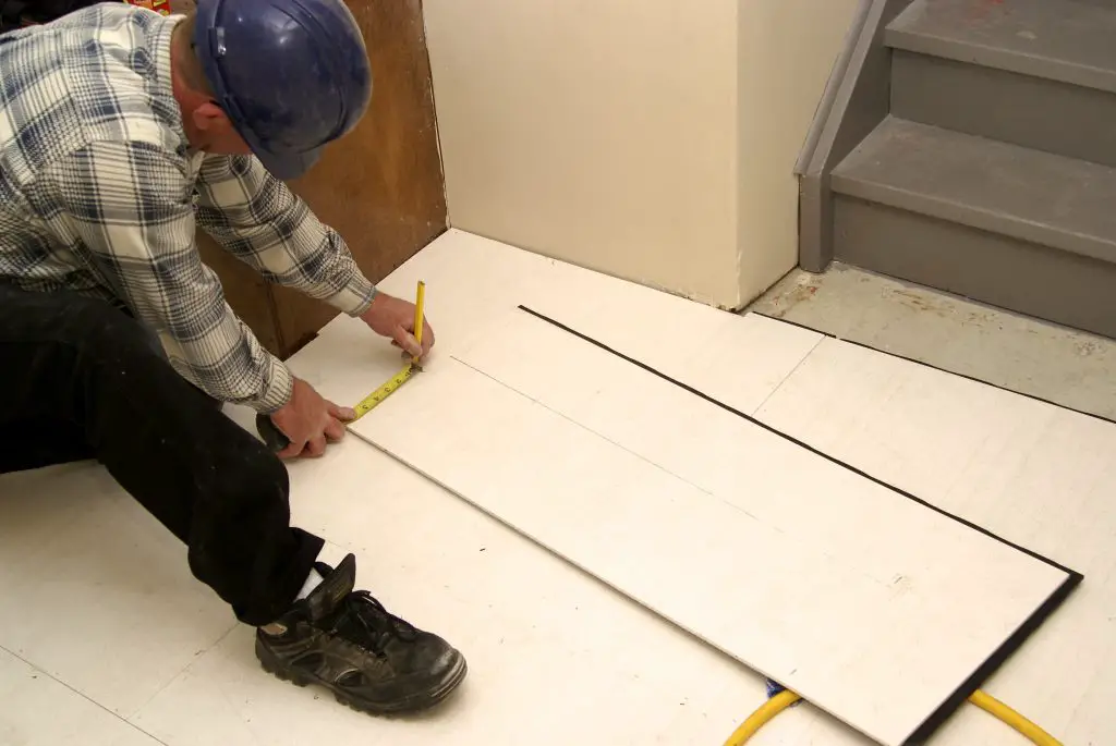 Worker measuring floor tiles near stairs.